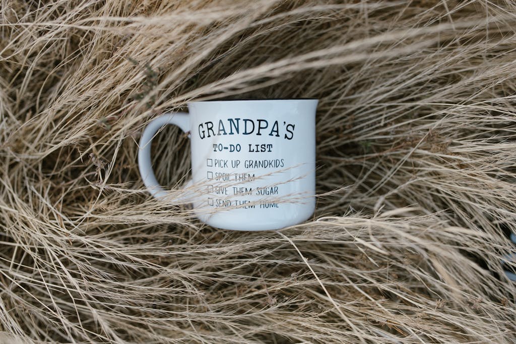 A playful Grandpa's to-do list mug nestled in dry grass, perfect for gifting a grandfather.